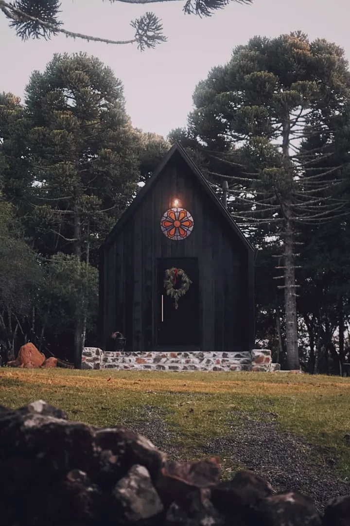 Fachada em A da cabana, com guirlanda na porta, entre as araucárias